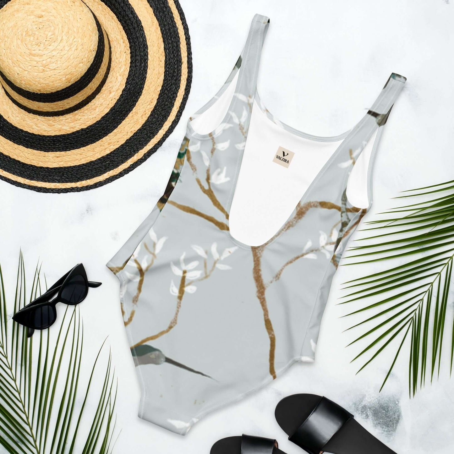 Costume da bagno intero con design floreale, ideale per la moda mare 2025, abbinato a cappello e accessori da spiaggia.