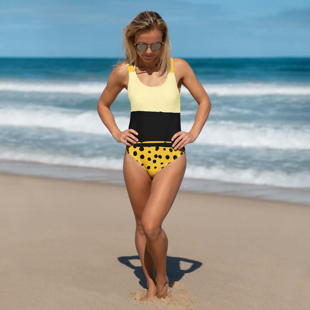 Donna in costume da bagno intero a pois gialli e neri sulla spiaggia, ideale per la moda mare 2025.
