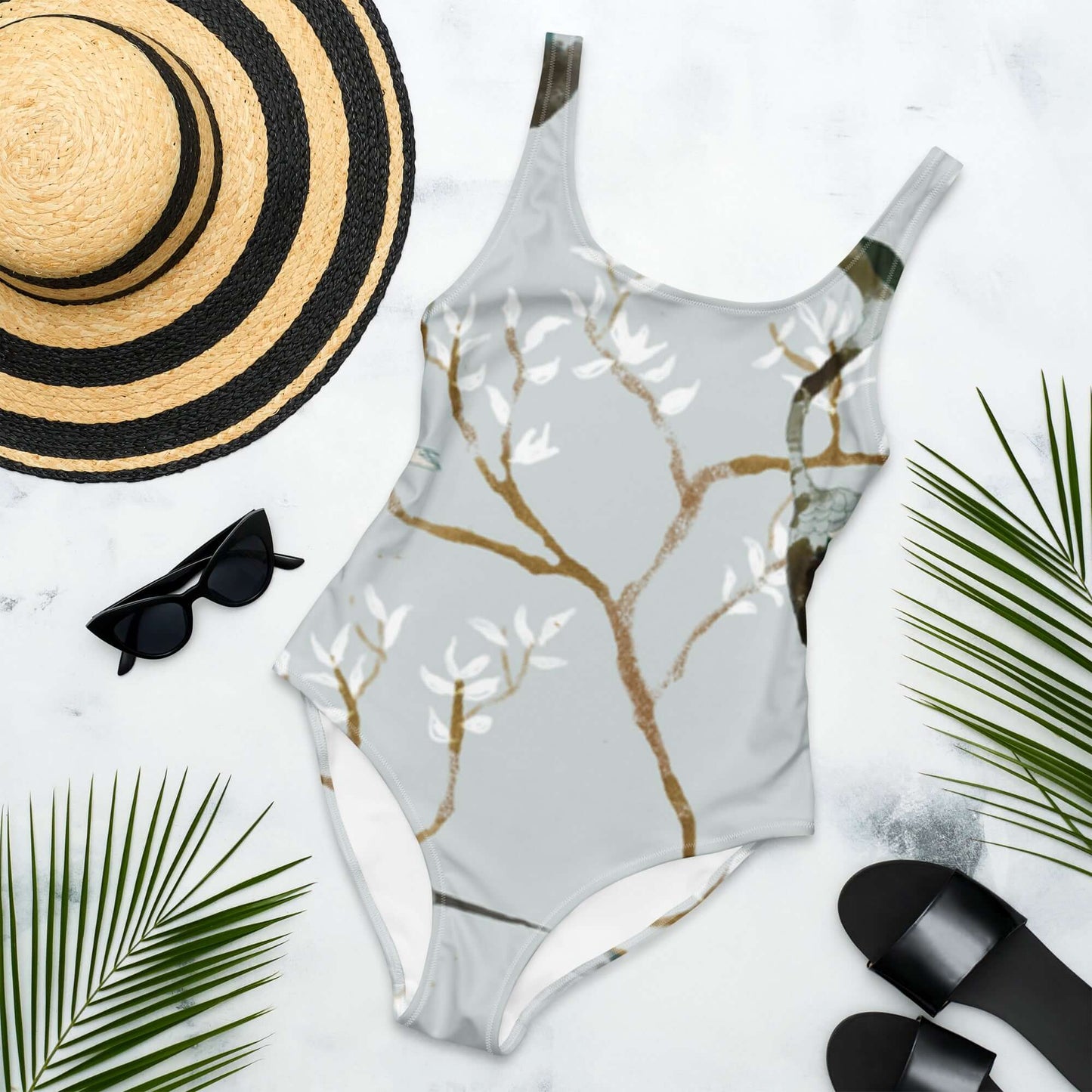 Costume da bagno intero con design floreale, occhiali da sole, cappello e infradito su sfondo estivo.